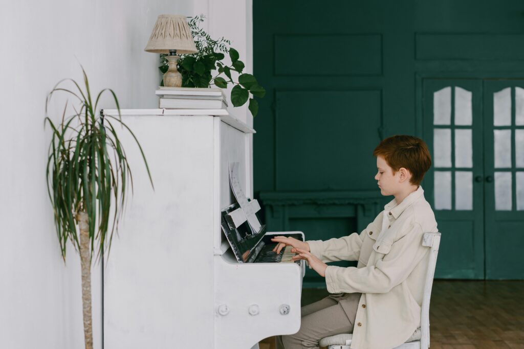 Young boy playing a piano indoors with plants surrounding, showcasing musical talent and lifestyle.