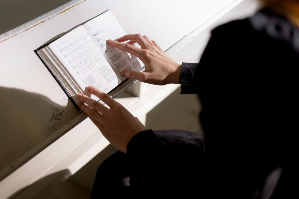 Close-up of hands on a hymnal page, illuminated by bright light indoors.