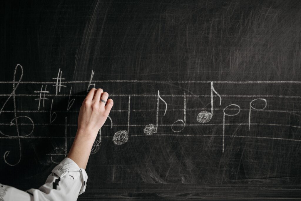 Is Music Theory Still Important in the Age of AI and Social Media? A person writing musical notes on a blackboard with chalk indoors.